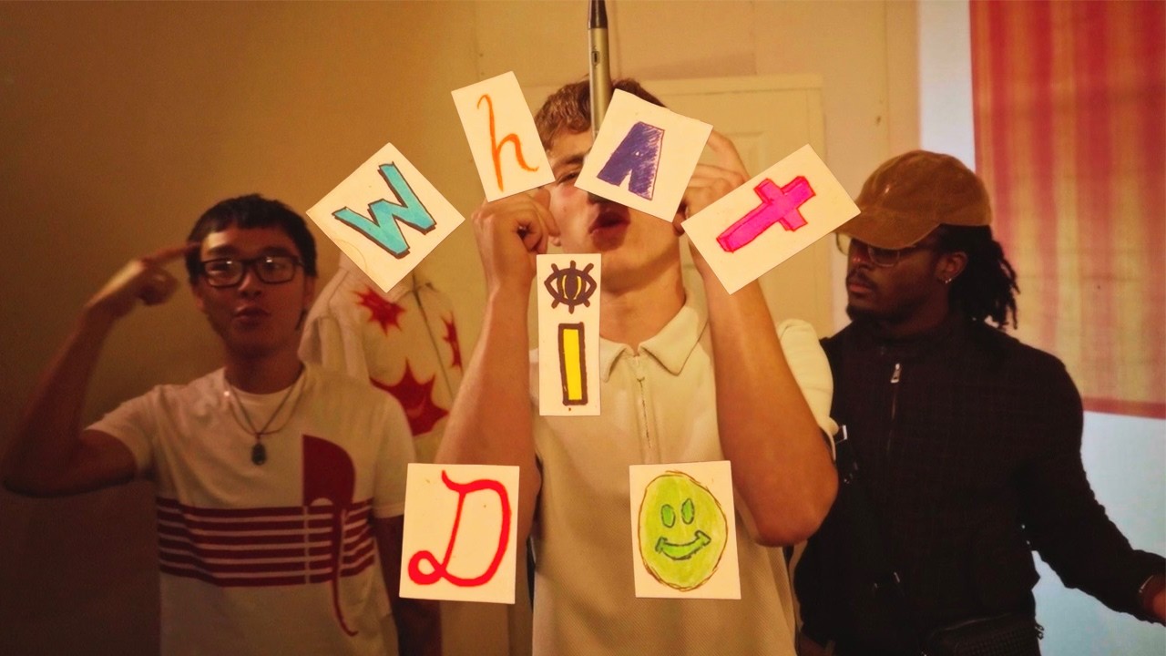 Still from the What I Do video: rockylevi at a hanging mic holding hand-drawn letter cards